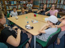 Dzieci siedzą przy stole, a chłopiec prezentuje pracę robota zdalnie sterowanego