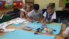 Dzieci siedzą przy stole i wycinają elementy prac
