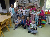 Grupa dzieci z panią bibliotekarką przed regałem z ich pracami