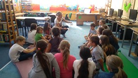 Dzieci siedzą na materacach a bibliotekarka tłumaczy dzieciom zasady