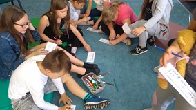 Dzieci siedzą na materacach i wykonują wizytówki