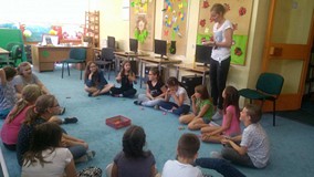 Dzieci siedzą w kole a bibliotekarka tłumaczy im zasady gry