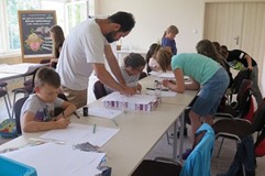 Dzieci pracują nad  komiksem, podczas gdy pan Artur tłumaczy im techniki właściwego redagowania komi