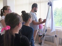 Pan Artur rysuje po tablicy, a dzieci obserwują go stojąc wokół niego