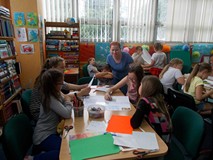 Grupa dzieci jest w trakcie tworzenia wspólnego plakatu o tygrysach, a biibliotekarka wspiera ich pr