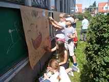 Dzieci malują farbami na papierze pocztowym zawieszonym na budynku