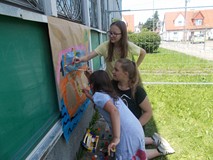 Trzy dziewczynki kolorują naszkicowany statek za pomocą farb plakatowych