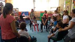 Dzieci siedzą na krzełach w kręgu, a bibliotekarka bawi się w z nimi w oczko