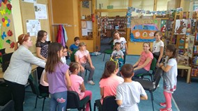 Dzieci siedzą na krzesłach w kręgu, a bibliotekarka prowadzi zabawę