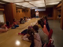 Bibliotekarka opowiada dzieciom siedzącym przy stołach o twórczości Małgorzaty Strękowskiej-Zaremby