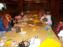 Dzieci siedzą przy wspólnym stole tworząc notesy na autografy