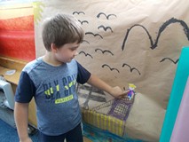 Chłopiec przykleja pirata do pracy plastycznej z wizerunkiem statku