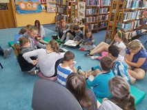 Dzieci siedza kole i czytają na głos