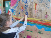 Dziewczynka przykleja zdjęcia do pracy na której znajduje się statek