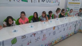 Dzieci siędzą przy stołach wykonując doświadczenia