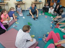 dzieci siedzą w kole słuchąc bibliotekarki, która prowadzi grę
