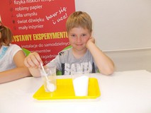 Chłopiec siedzi przy stole wykonując doświadczenia