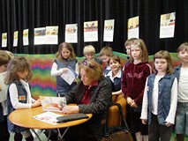 Przy stoliku siedzi pani Wanda Chotomska i podpisuje książkę w otoczeniu dziesiątki dzieci po spotka