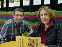 Przy stoliku siedzi pani Wanda Chotomska i podpisuje książkę dorosłemu czytelnikowi po spotkaniu w s