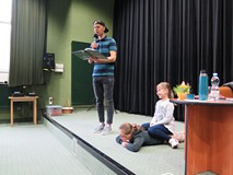 W zcasie spotkania autorskiego na scenie stoi pisarz Przemysław Wechterowicz ubrany po młodzieżowemu