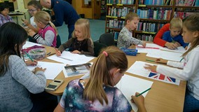 Dzieci siedzą przy stole i wykonują prace plastyczne