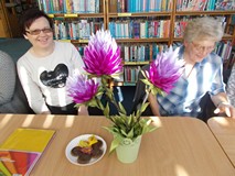 Dwie Panie pozują do zdjęcia z wykonanym przez jedną z nich kwaitem z kolorowych tasiemek