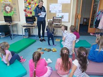 Dzieci siedzą przed bibliotekarką, która pokazuje im obrazy najsłynniejszych malarzy