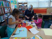 Dzieci siedzą przy stole i tworzą obraz, a rodzic wspiera ich pracę