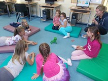 Dzieci wraz z bibliotekarką siedzą na materacykach i grają w grę ręka, która mnie nie nęka