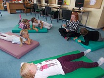 Bibliotekarka czyta fragment książki dzieciom siedzącym na materacykach