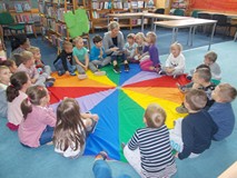 Bibliotekarka czyta książkę dzieciom, które siedzą na chuście animacyjnej