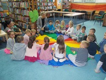 Dzieci siedza na chuście animacyjnej i odpowiadają na pytania bibliotekarki