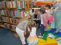 Bibliotekarka przykleja rysunki dzieci do wyciętego z papieru drzewa