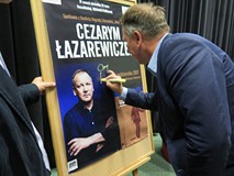 Cezary Łazarewicz składa autograf na plakacie promującym spotkanie