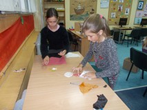 Dwie dziewczynki stoją przy stole i wycinają elementy pracy