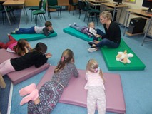 Dzieci leżą na materacykach i słuchają baśni czytanej przez bibliotekarkę