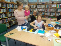 Dzieci wykonują swoje prace, a mała dziewczynka na rękach cioci obserwuje z zaciekawieniem co robią 