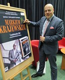 Marek Krajewski składa autograf na plakacie promującym spotkanie