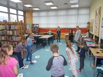 Dzieci patrzą z zaciekawieniem na bibliotekarkę trzymającą wylosowanę przez siebie kartkę z nazwą za